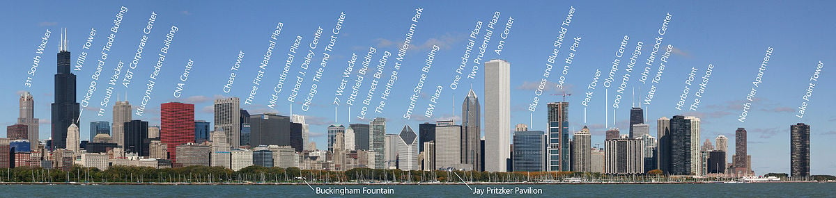 The skyline of a city with many large skyscrapers; in the foreground are a green park and a lake with many sailboats moored on it. Over 30 of the skyscrapers and some park features are labeled.