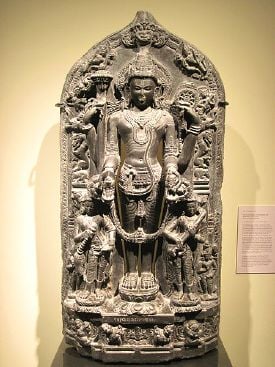 12th century stone sculpture of God Vishnu flanked by two apsaras one with a fan (left) and the other with Tambura (right).