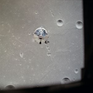 O topo do módulo de comando prateado é visto em uma superfície lunar cinza com crateras.