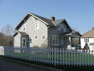 Gray clapboard house, surrounded by a white picket fence
