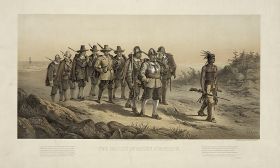 A group of nine 17th century militiamen carrying muskets and marching over a sandy path. A Native American man is leading them, with feathers in his hair and carrying a musket. The soldier at the front of the group is wearing a helmet and a breastplate. In the background is a beach.