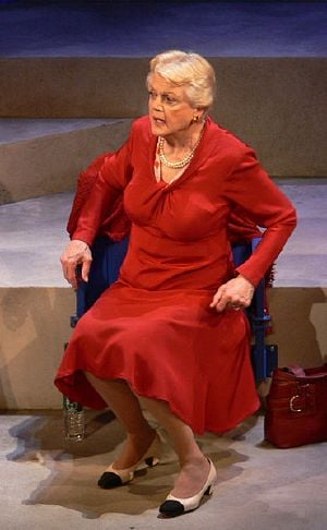 An elderly white woman wearing a red dress sitting in a chair