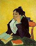 An intense woman with black hair, elbow rests on a table of books and stares to the left.