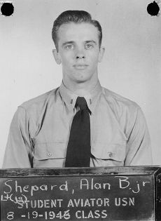 Shepard, in Navy uniform short and tie, stands before a blackboard on which is stencilled "Student aviator USN – 8-19-1946 class. Above that is written in chalk: "Lt (jg) Shepard, Alan B. Jr"